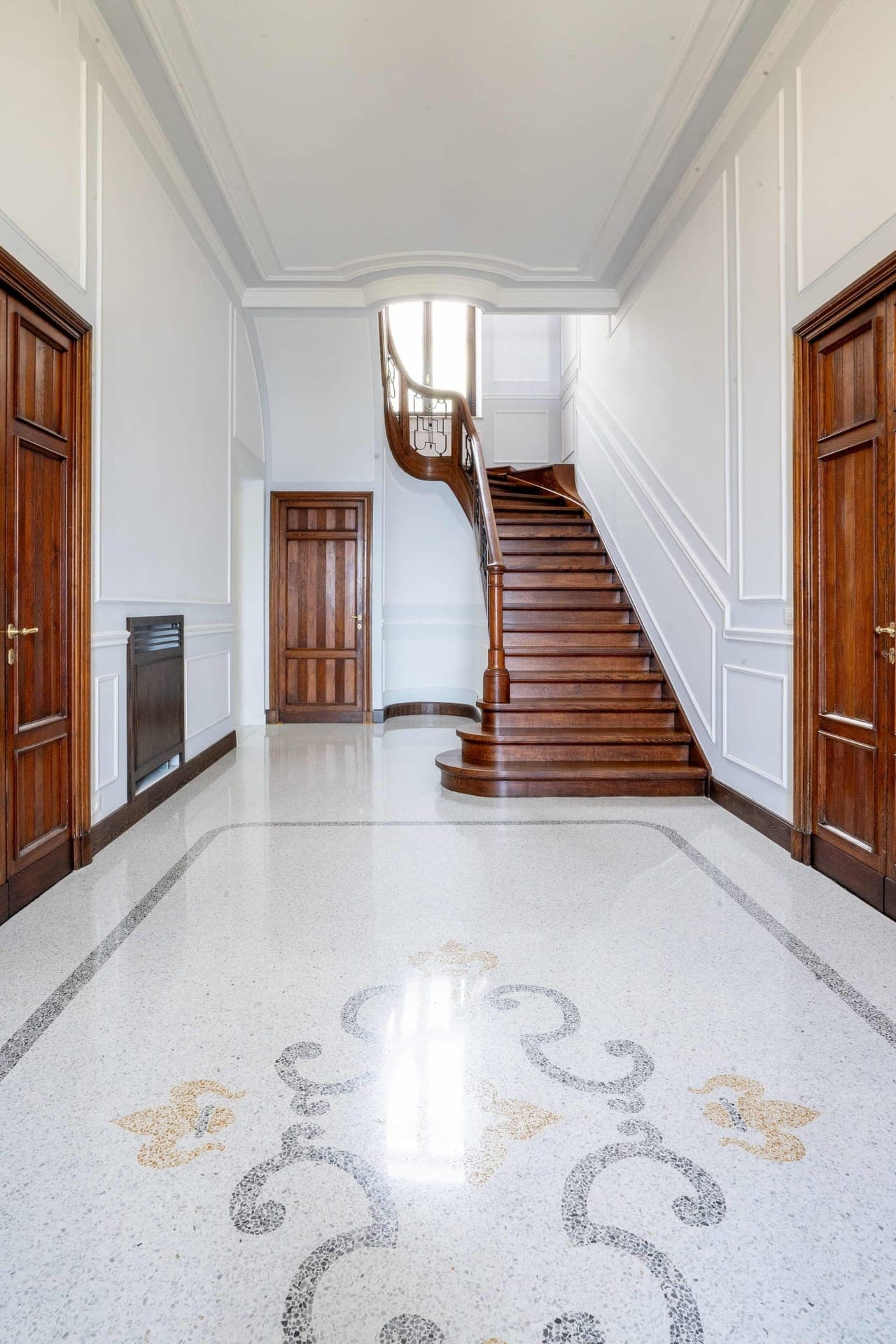 Grand entrance hall with decorative terrazzo floor and sweeping wooden staircase