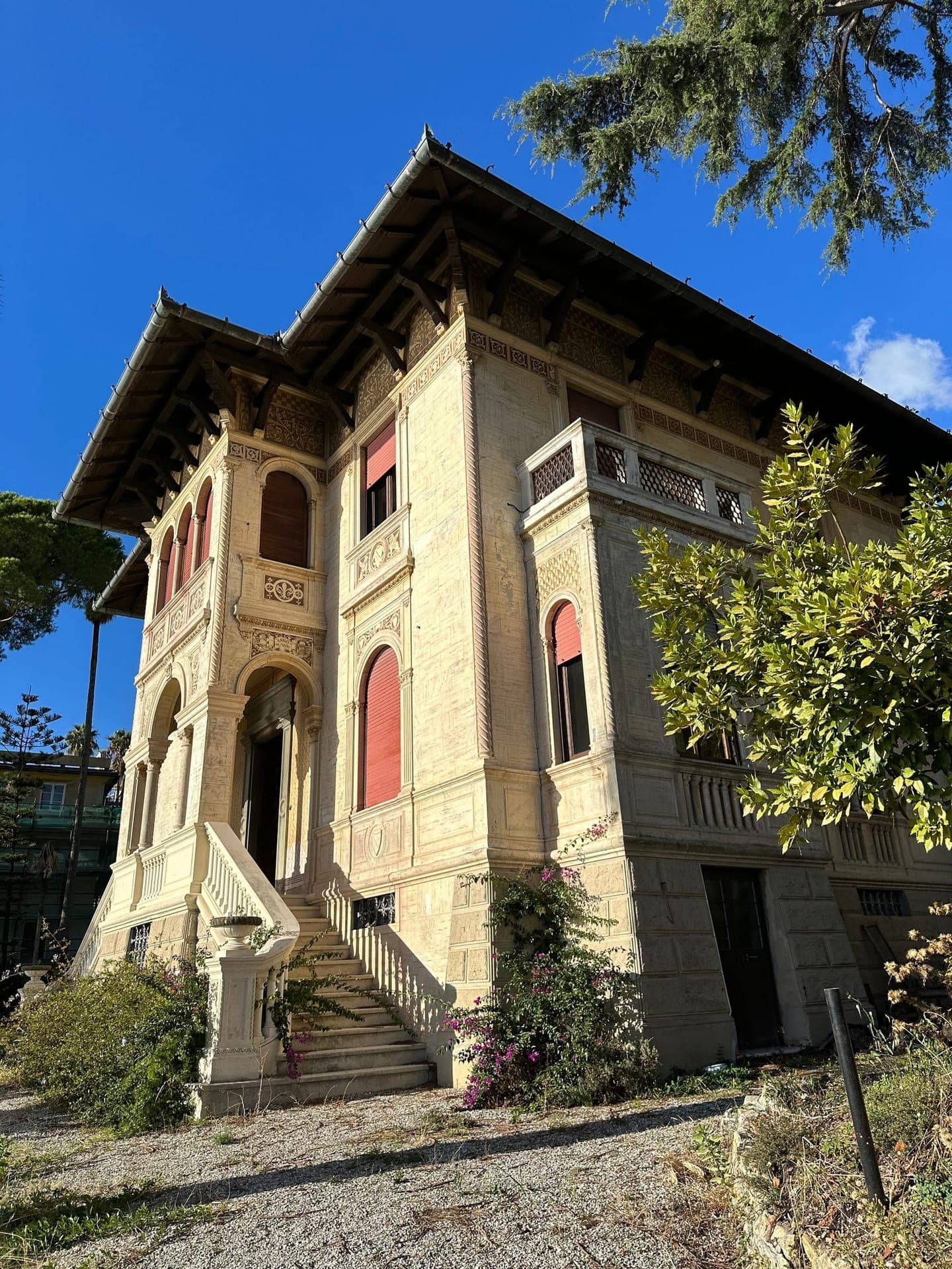 The ornate frescoed facade of La Villa Italiana with arched windows, coral shutters and a grand external staircase against a blue sky
