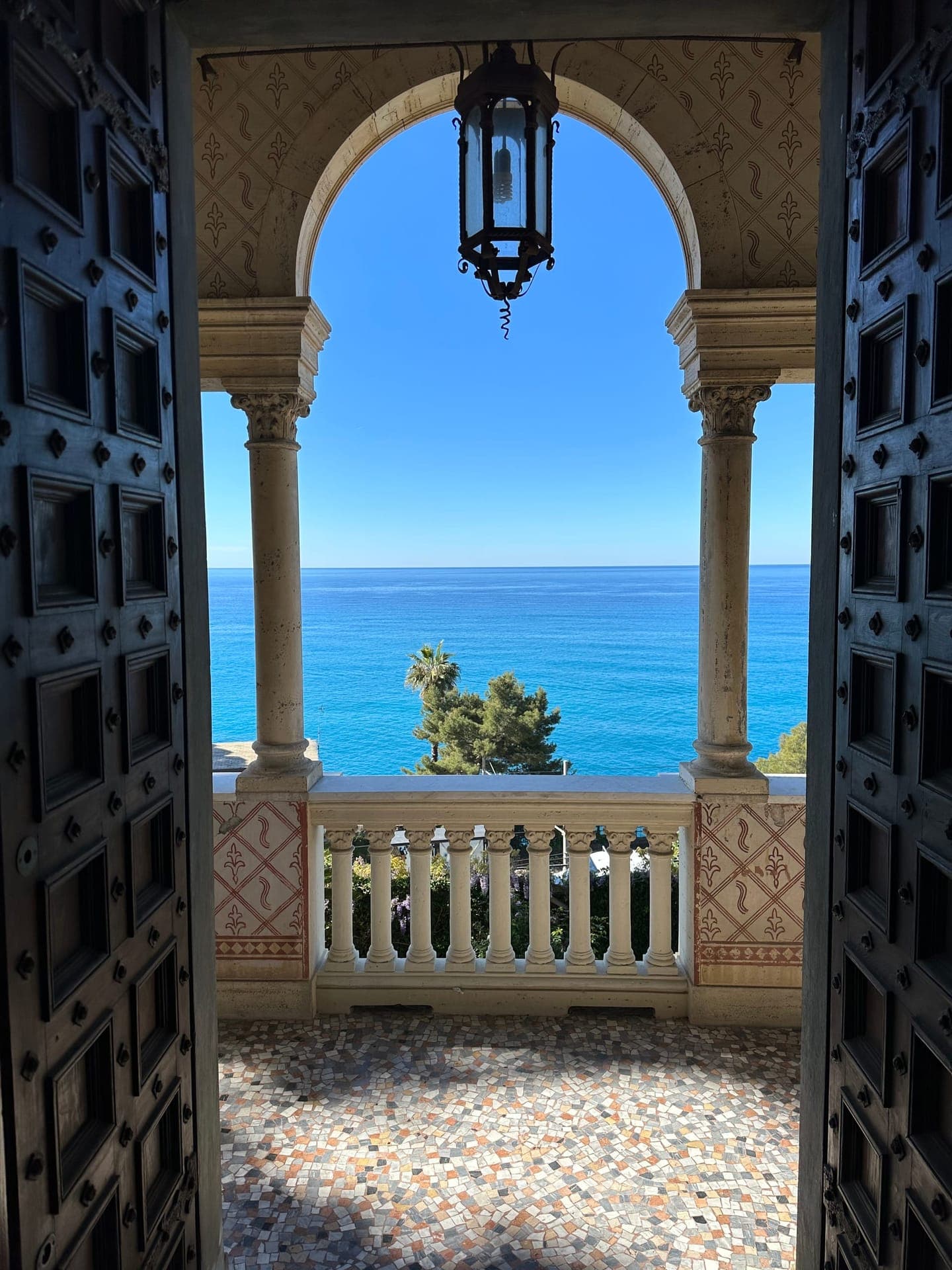 View of the Mediterranean sea through the villa's arched seafront loggia with painted columns and a mosaic terrace