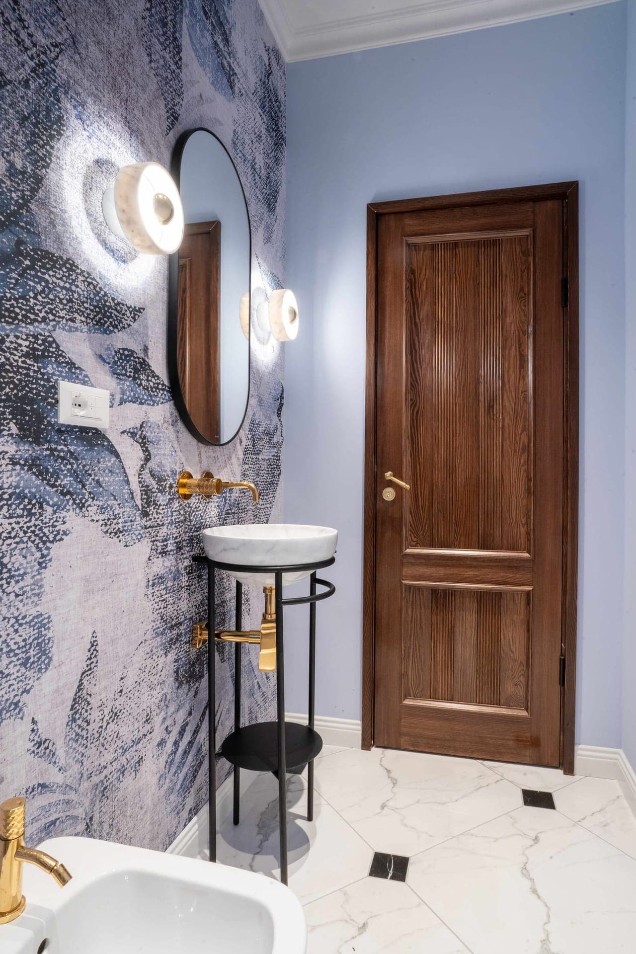 Powder room with abstract blue wallpaper, round mirror and marble basin