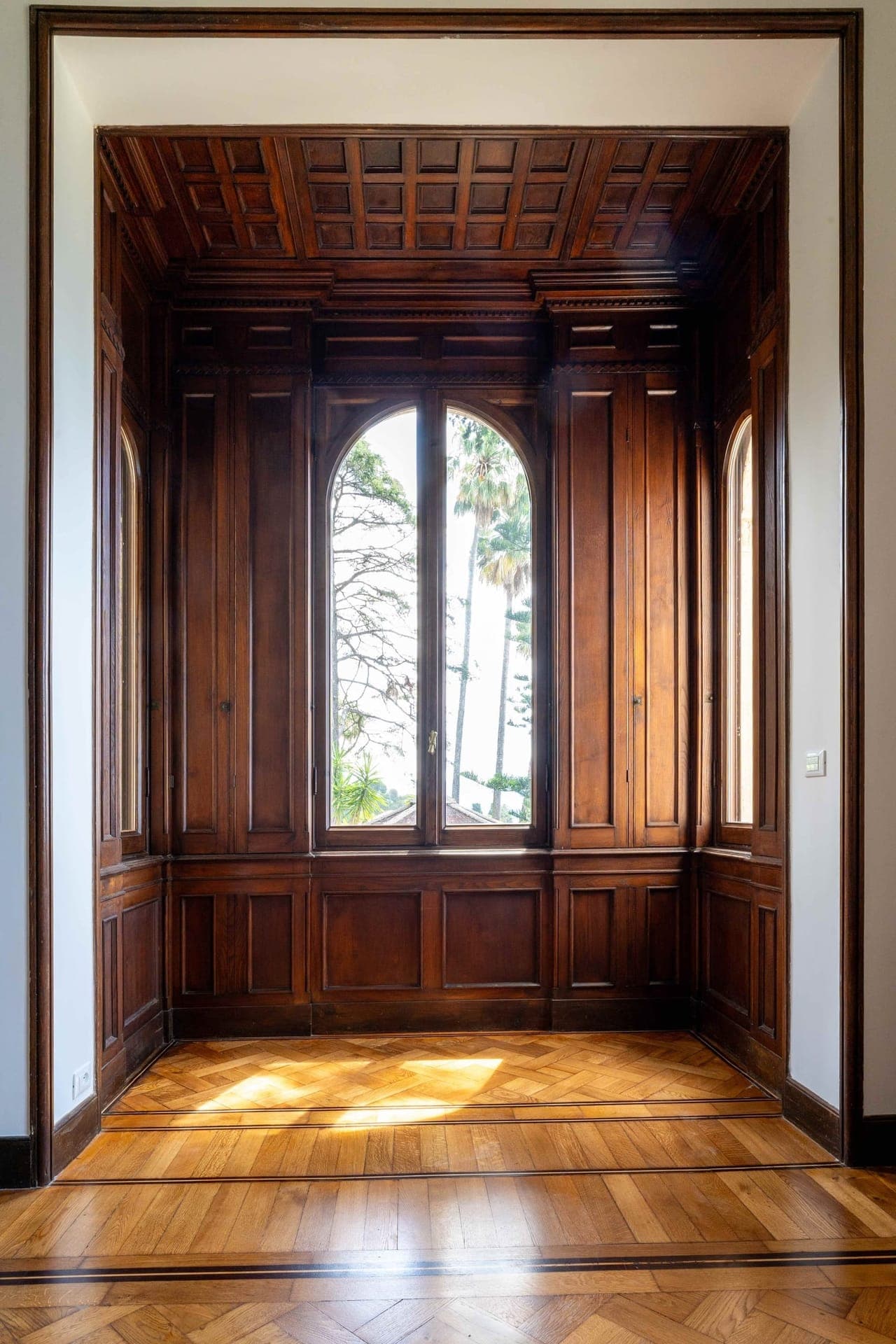 Wood-panelled reading alcove with coffered ceiling and arched garden window